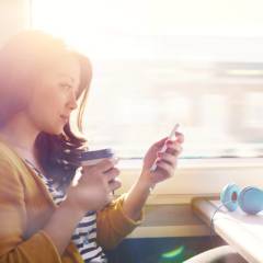 Frau sitzt im Zug und hält ein Handy in der Hand