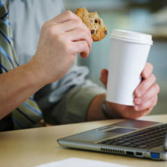 Mann mit Keks und Kaffee vor dem Laptop