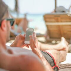 Ein Mann mit Basecap liegt auf Strandliege und schaut auf sein Smartphone