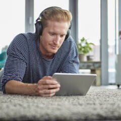 Amazon Prime Video Tipps Symbolbild: Junger Mann liegt mit Kopfhörern und Tablet auf dem Boden